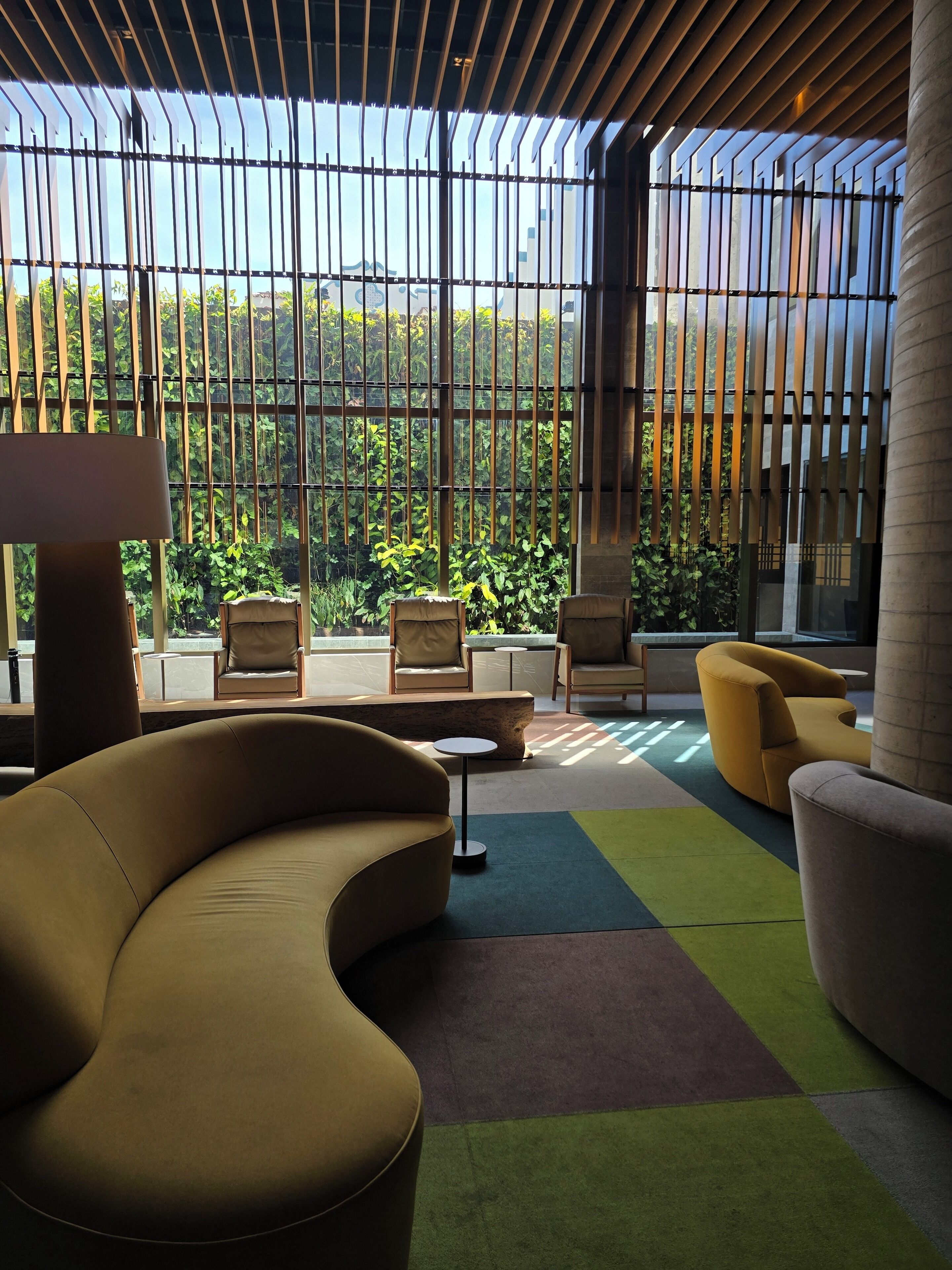 Un espacio lounge moderno con un sofá curvo, sillones y una pequeña mesa. Amplias ventanas dejan entrar luz natural y ofrecen vistas a la vegetación.