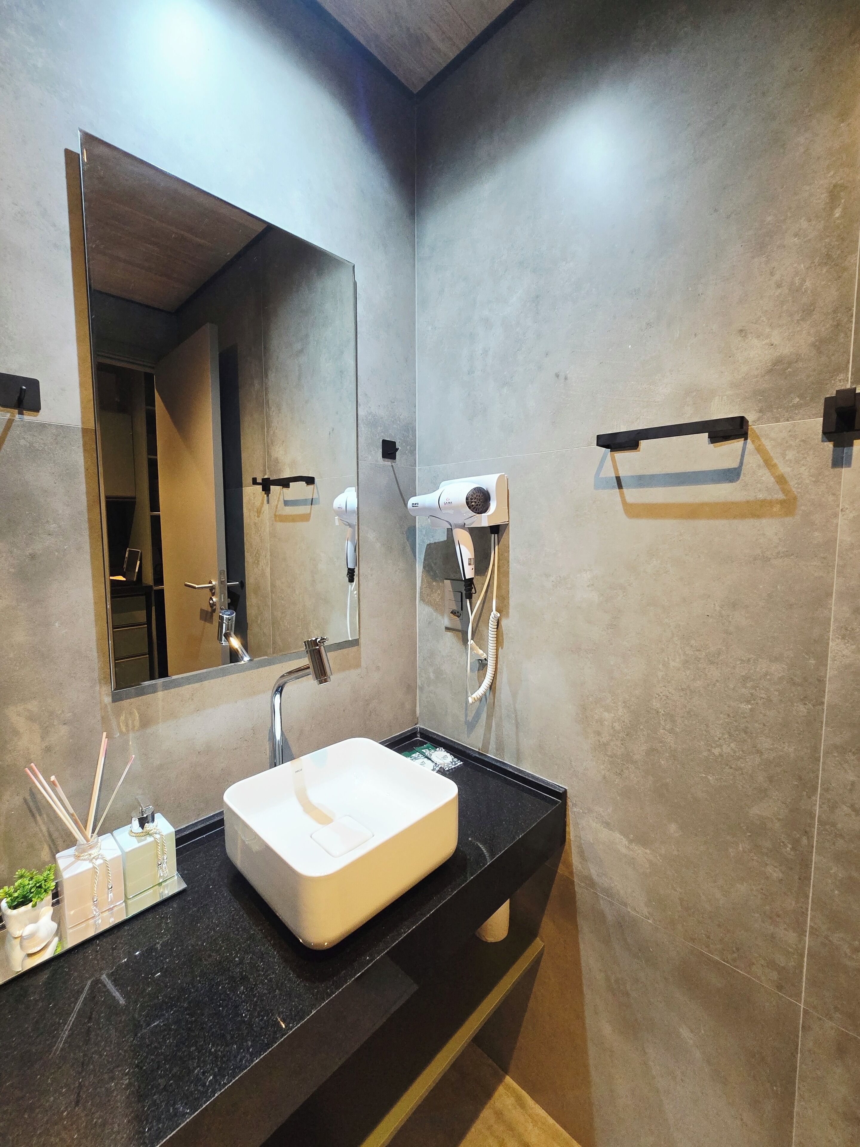 Casa de banho moderna com um espelho grande, uma sanita branca e um secador de cabelo fixado na parede.