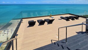 Eine Dachterrasse mit freiem Blick auf das Meer, Liegestühlen und einer Glasuferung.