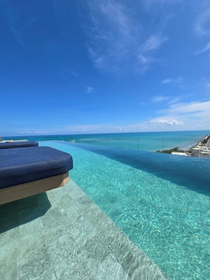 A clear blue sky, a swimming pool, and a lounge area with a view of the ocean.
