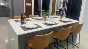 Uma cozinha moderna com uma ilha central, armários cinzas e uma área de jantar com uma mesa branca posta para quatro pessoas.