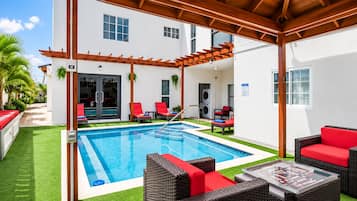 Un espace aménagé au bord de la piscine, comprenant une piscine rectangulaire, des sièges d’extérieur et une pergola couverte.