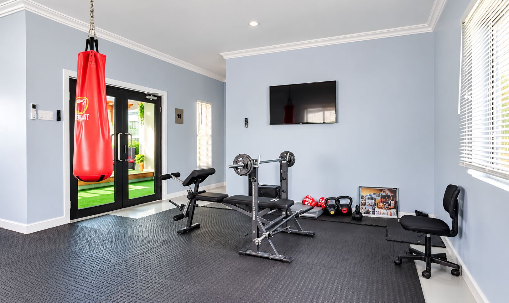 Ein Heimfitnessraum mit einem Sandsack, einer Gewichtbank, einem Squat-Gestell und Kettlebells.