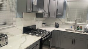 Uma cozinha moderna com armários cinza, fogão a gás, forno embutido e janela com persianas.