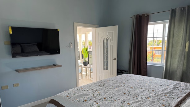 Quarto com cama, televisão na parede, porta para uma varanda e janela com cortinas.