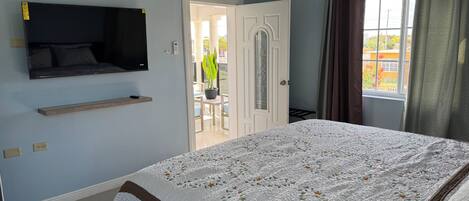 A bedroom with a bed, a mounted TV, a door leading to a balcony, and a window with curtains.