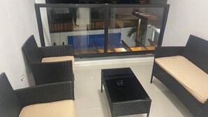 Varanda com mobiliário de vime, uma mesinha e vista para o exterior.