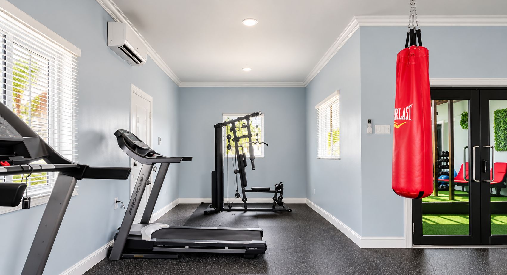 Une salle de sport à domicile équipée d’un tapis de course, d’un banc de musculation et d’un sac de frappe.