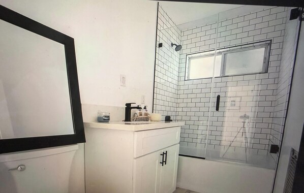 Et badeværelse med hvidmalede vægge, et hvidt toiletbord med spejl, en bruser og et vindue.