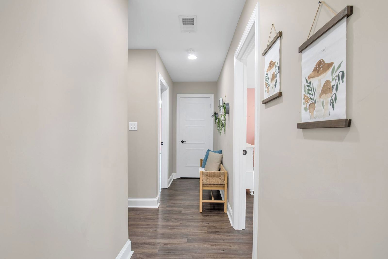A hallway with a door at the end, a chair with cushions, and two framed pictures on the wall.