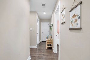 A hallway with a door at the end, a chair with cushions, and two framed pictures on the wall.