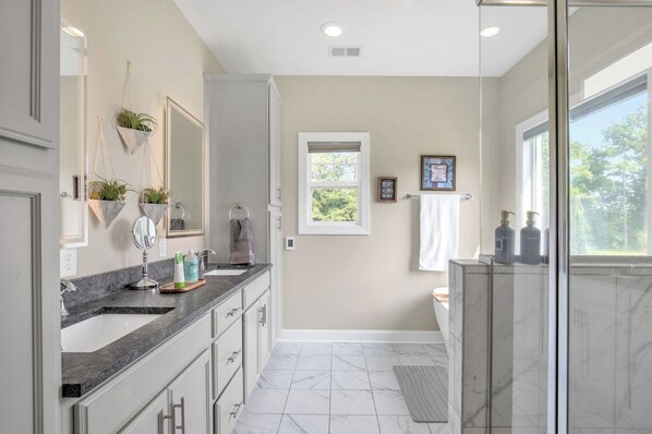 A modern bathroom with a marble sink, a glass shower enclosure, and a window providing natural light.
