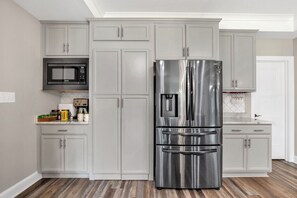 Una cocina con armarios grises, un refrigerador de acero inoxidable, un microondas y un salpicadero de azulejos.