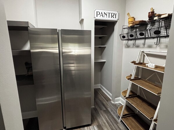 A compact kitchen with a stainless steel refrigerator, a pantry area, and open shelving with kitchenware.