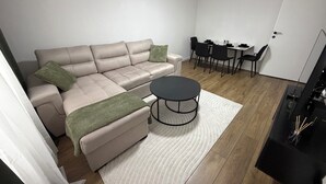 A modern living room with a sofa, ottoman, coffee table, and dining area with chairs and a table.