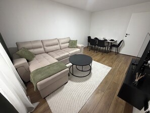 A modern living room with a sofa, ottoman, coffee table, and dining area with chairs and a table. - Sarajevo, Stan Sarajevo, DINE Apartment, Sarajevo Apartment (Sarajevo)