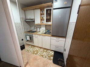Una cocina compacta con refrigerador de acero inoxidable, estufa a gas y horno empotrado.