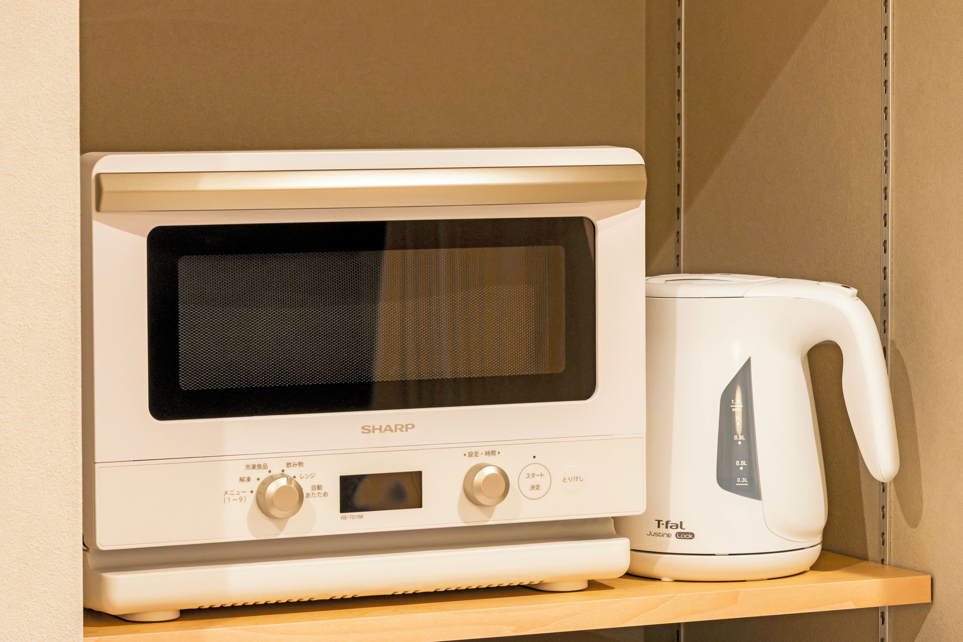 Un horno microondas con pantalla digital y panel de control, junto a una tetera eléctrica blanca sobre un estante de madera.