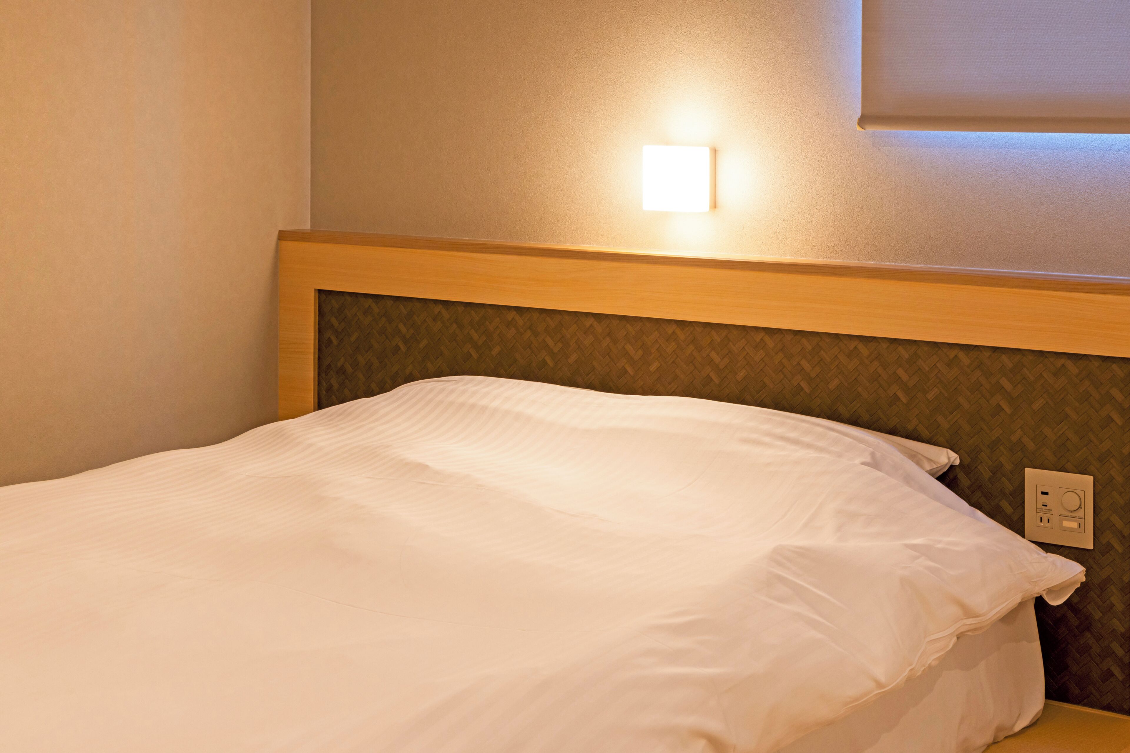 A single bed with a wooden headboard and a wall-mounted light fixture above it.