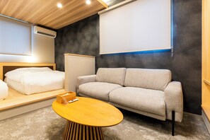 Una habitación de hotel moderna con sofá, una mesa de centro de madera, cama y aire acondicionado instalado en la pared.