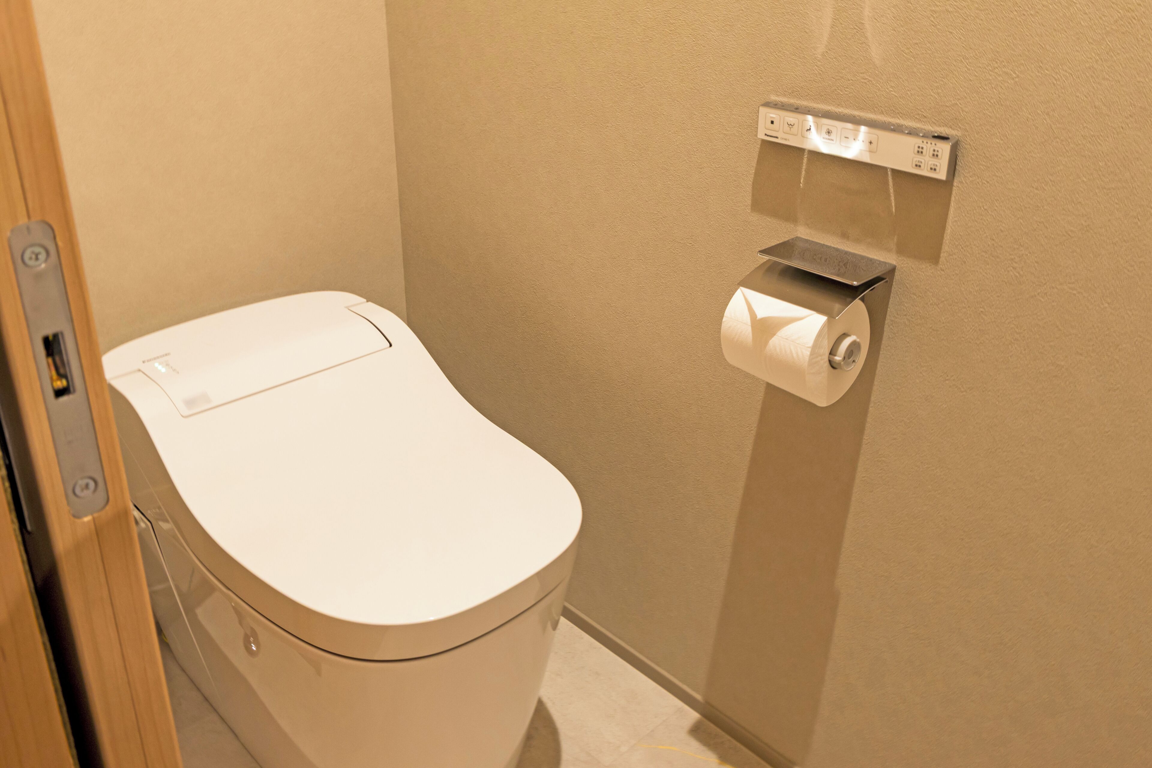 Un inodoro con una palanca de descarga, un dispensador de toallas de papel y un enchufe en la pared.