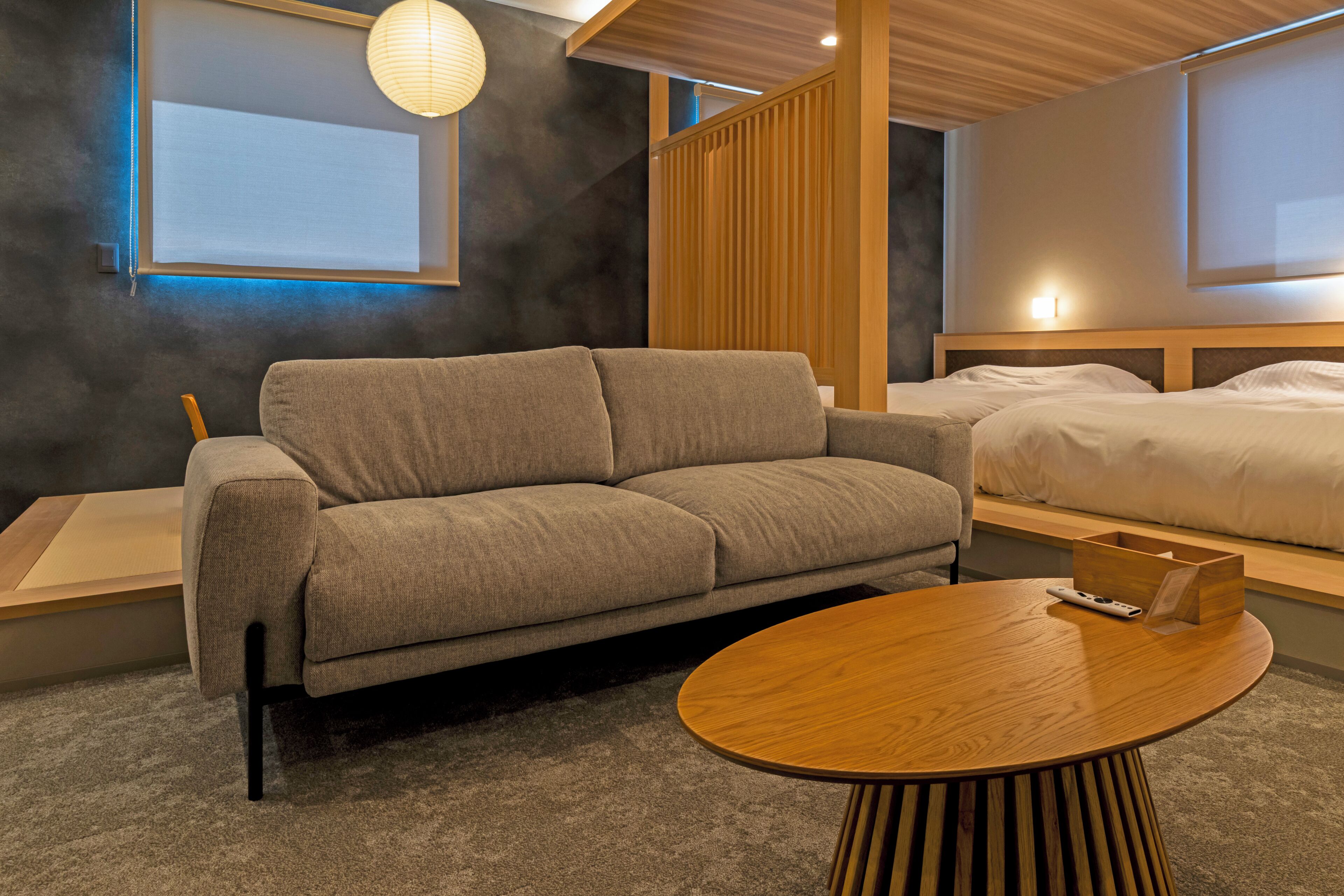 Una habitación de hotel moderna con un sofá, una mesa redonda de madera, una cama y vistas al exterior.