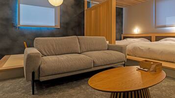 Una habitación de hotel moderna con un sofá, una mesa redonda de madera, una cama y vistas al exterior.