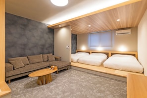 Una habitación de hotel moderna con un sofá, una mesita de centro de madera, una cama con ropa blanca y un techo con iluminación empotrada.