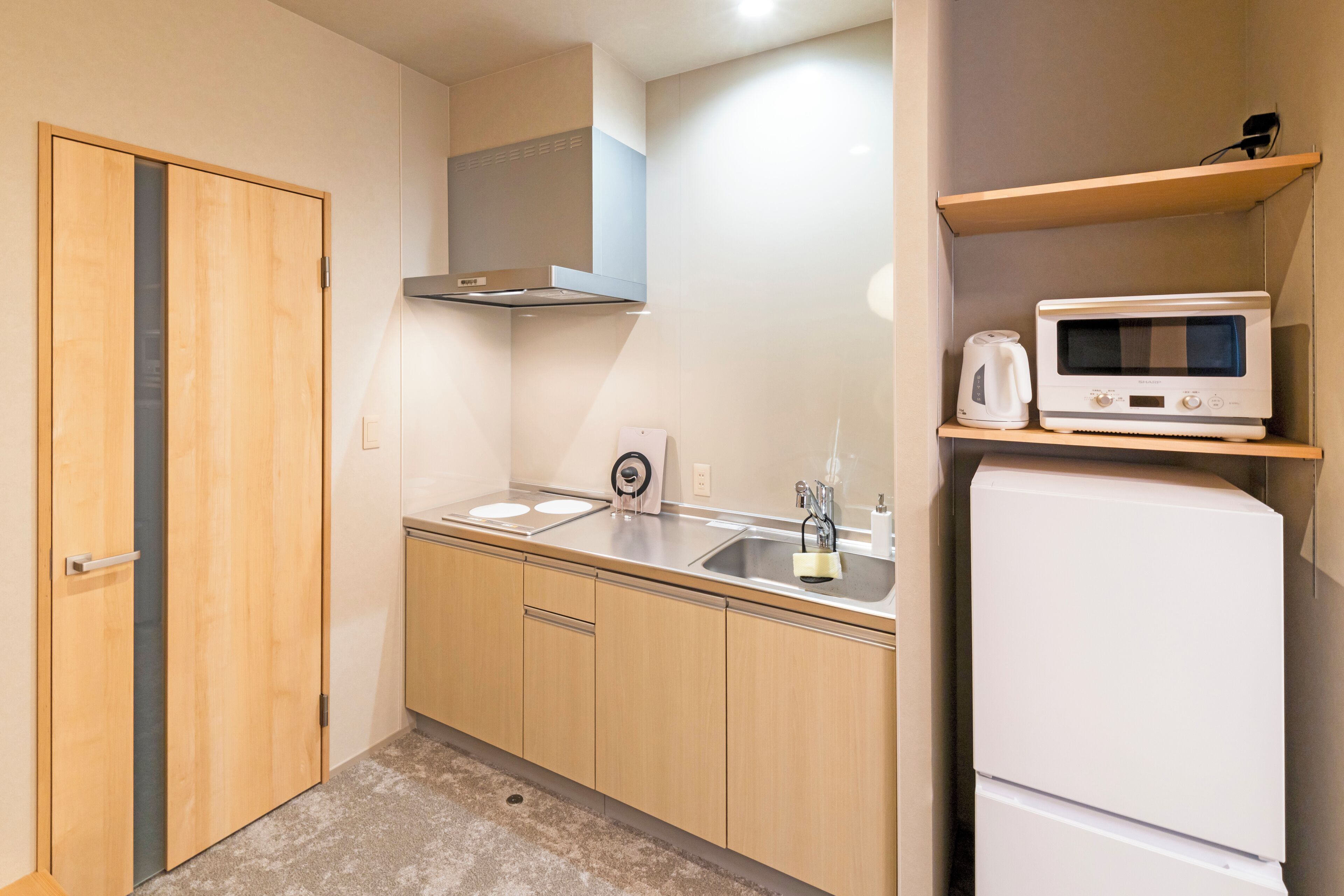 A compact kitchen with wooden cabinets, a stainless steel sink, a microwave, and a built-in oven.