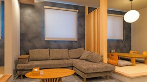 Una sala de estar moderna con un sofá seccional, una mesa de centro redonda de madera y una zona de comedor con mesa y sillas de madera.