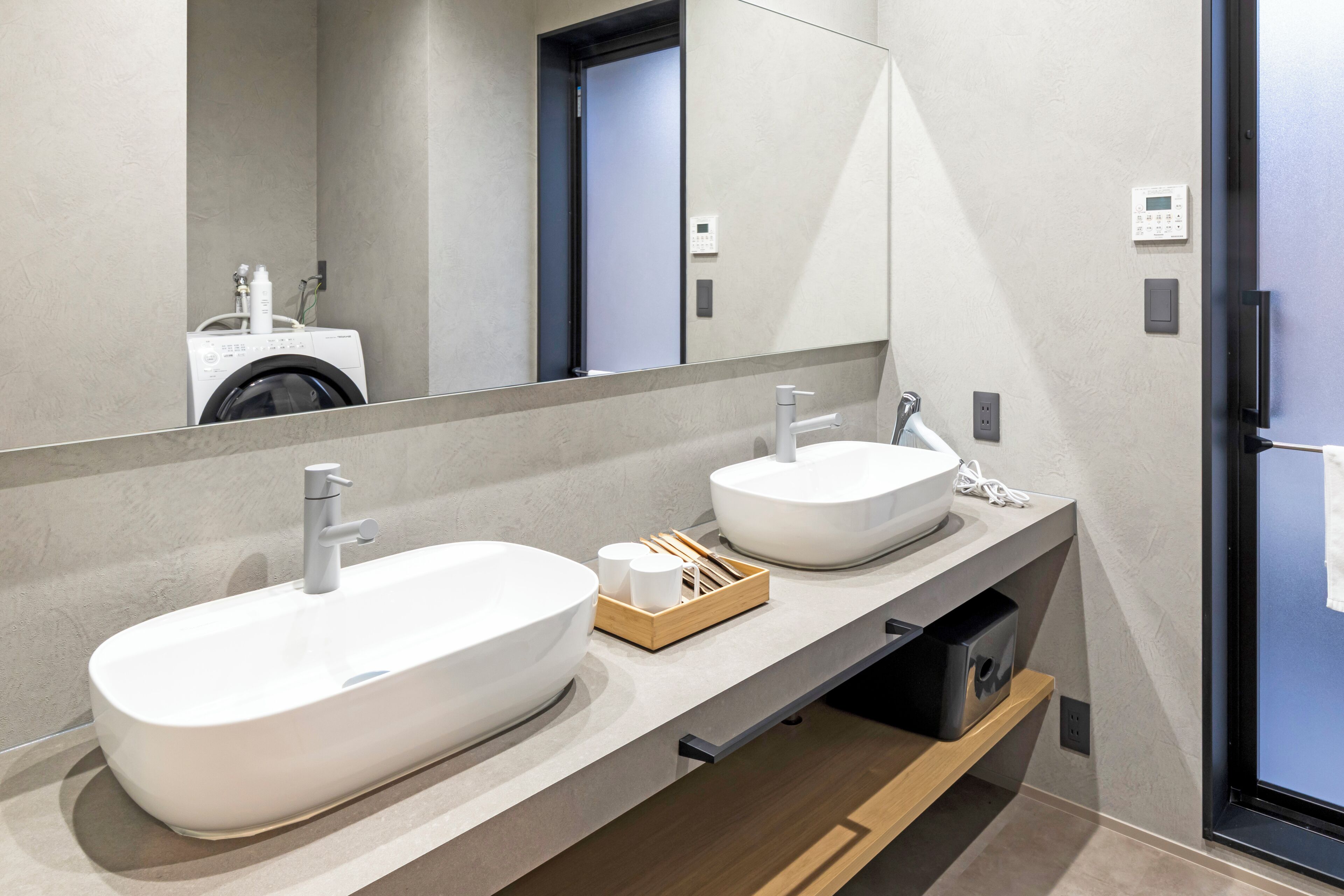 A modern bathroom with two sinks, a mirror, and a washing machine in the background.