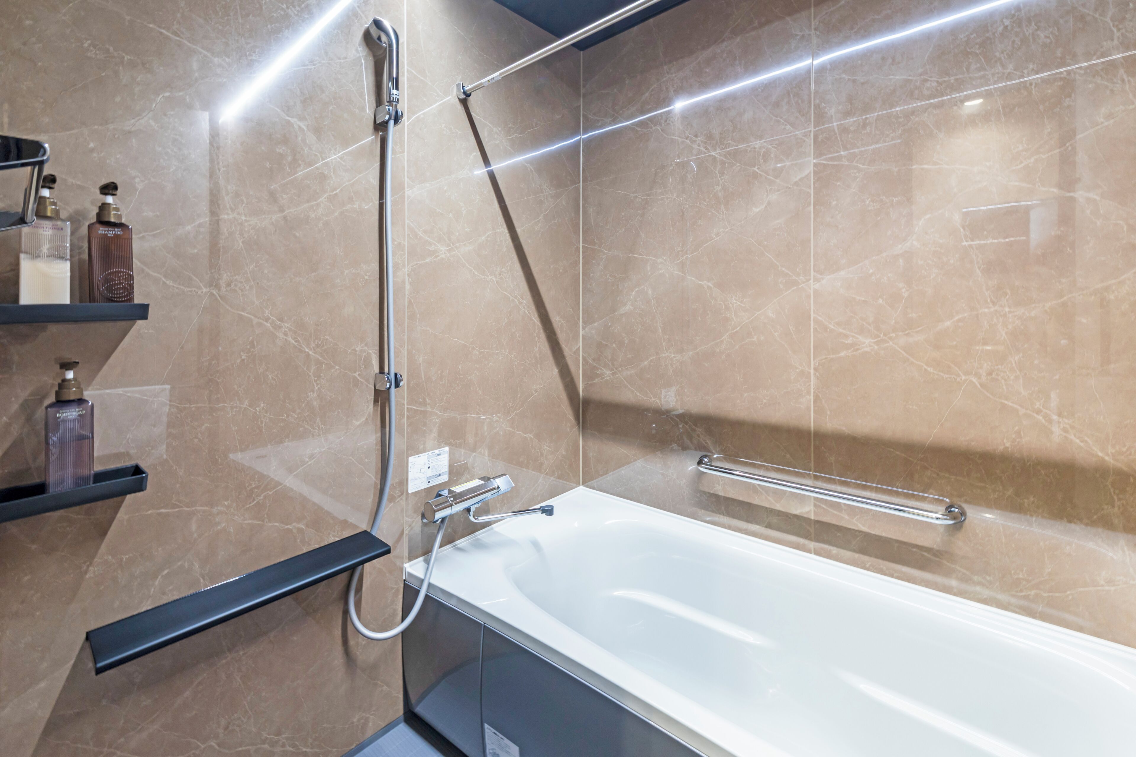 A modern bathroom with a white bathtub, a handheld showerhead, and a glass-enclosed shelf with toiletries.