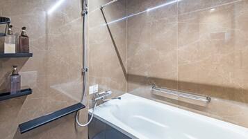 A modern bathroom with a white bathtub, a handheld showerhead, and a glass-enclosed shelf with toiletries.
