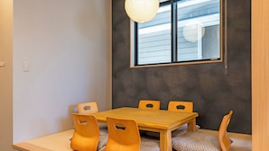 A dining area with a wooden table and matching chairs, a window with blinds, and a textured wall.