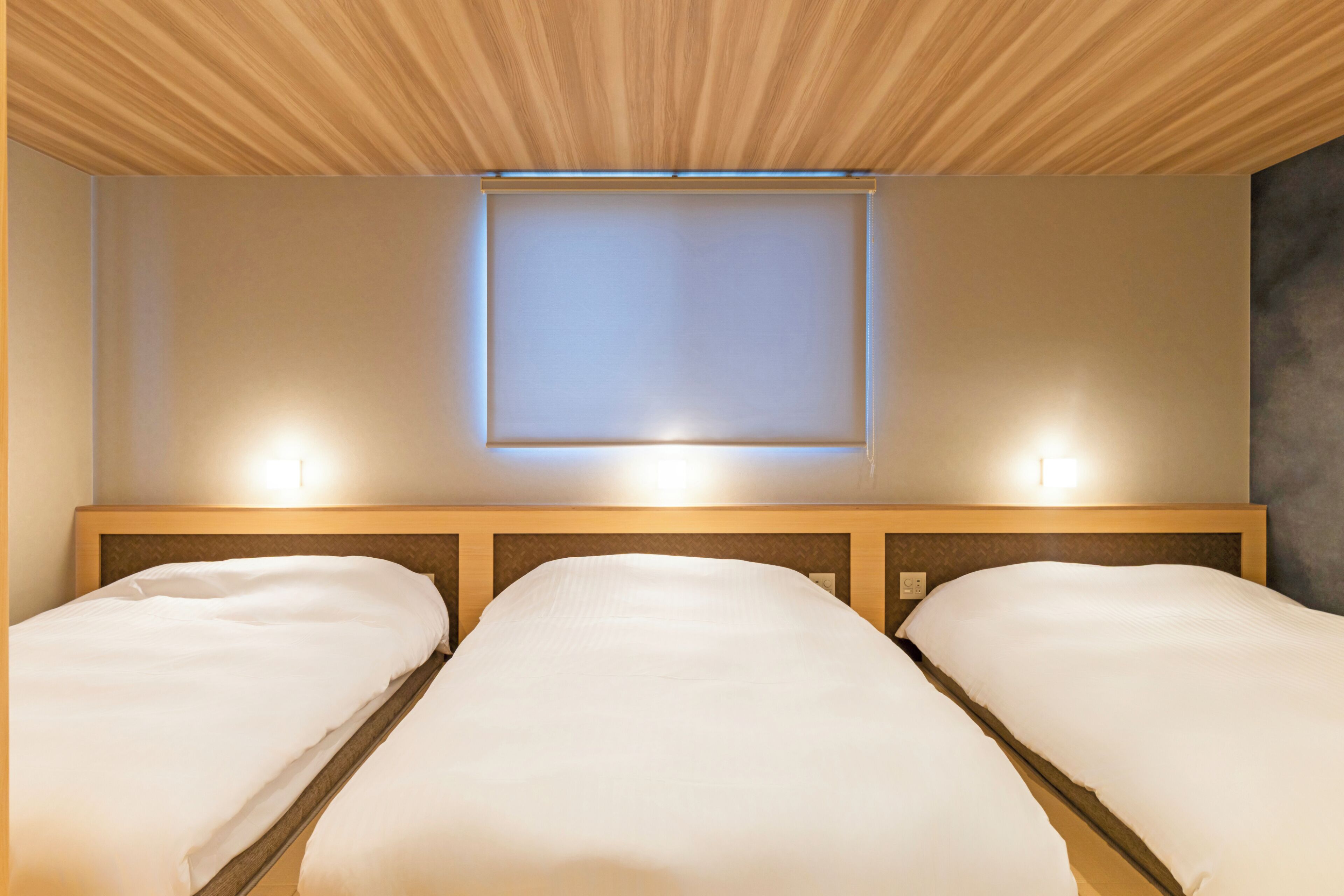 Une chambre d’hôtel avec deux lits, un plafond en bois et un luminaire fixé au mur.