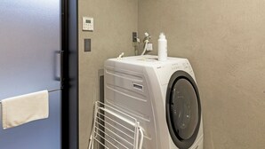 Una lavadora blanca compacta de carga frontal, un panel de control, una botella de detergente blanca y una toalla blanca colgada en un perchero.