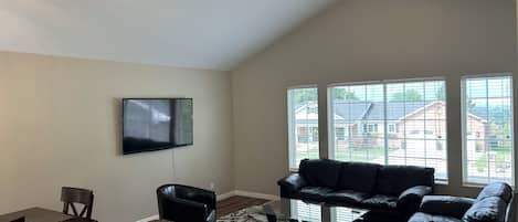 A living room with a flat-screen TV, a black leather sofa, a glass coffee table, and a patterned rug.