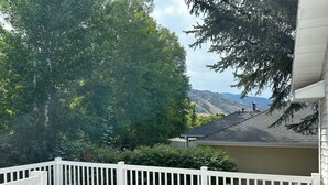 Eine Holzterrasse mit weißer Geländer, einem weißen Kunststoffstuhl und Blick auf ein Gebirge.