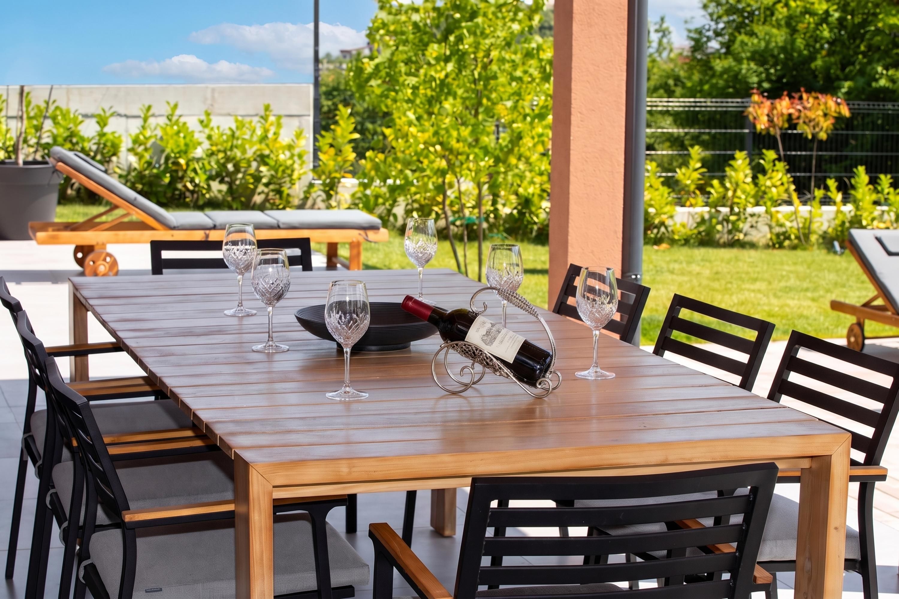 Un área de comedor al aire libre con una mesa de madera, sillas negras y copas de vino.