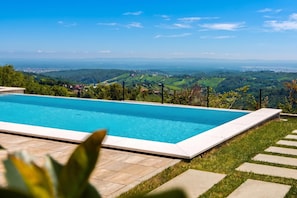 A rectangular swimming pool with a clear blue water surface, surrounded by a stone deck and a grassy area.
