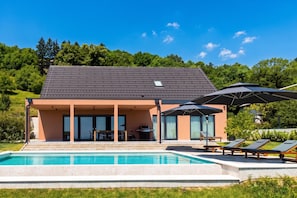A modern house with a swimming pool, outdoor seating, and a covered patio.