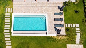 Vista aérea de una piscina con plataforma de cerámica, rodeada de césped y algunas sillas de descanso.