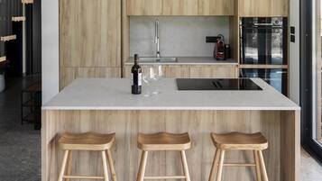 A modern kitchen with a central island, wooden stools, a wine bottle, and glasses.