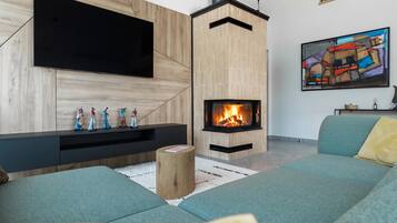 A modern living room with a flat-screen TV mounted on a wooden wall, a built-in fireplace, a sofa, and a colorful abstract painting.
