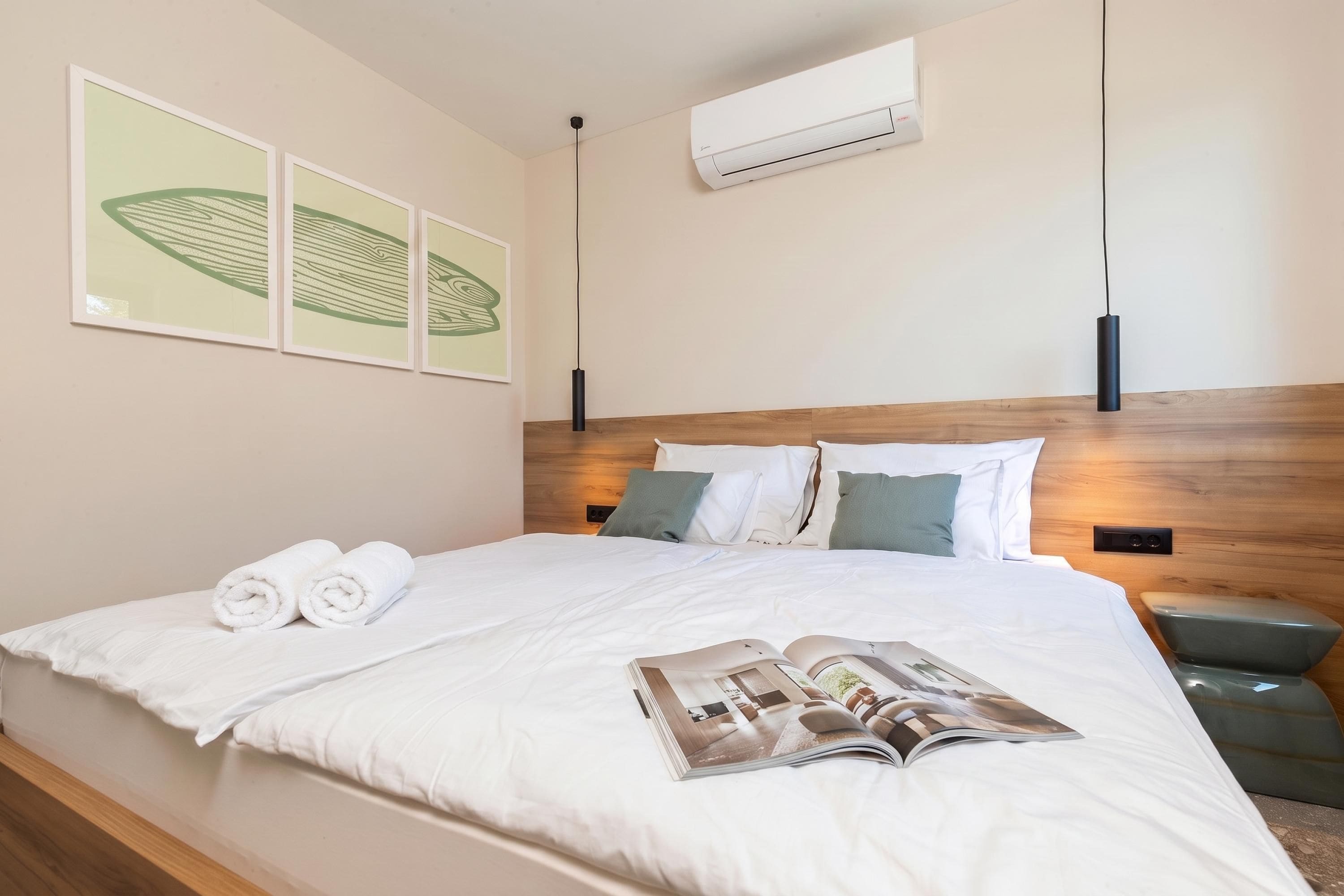A neatly made bed with white linens, a magazine, and rolled towels on the bed.