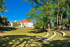 A park with a white building with a red roof, surrounded by trees and grass.