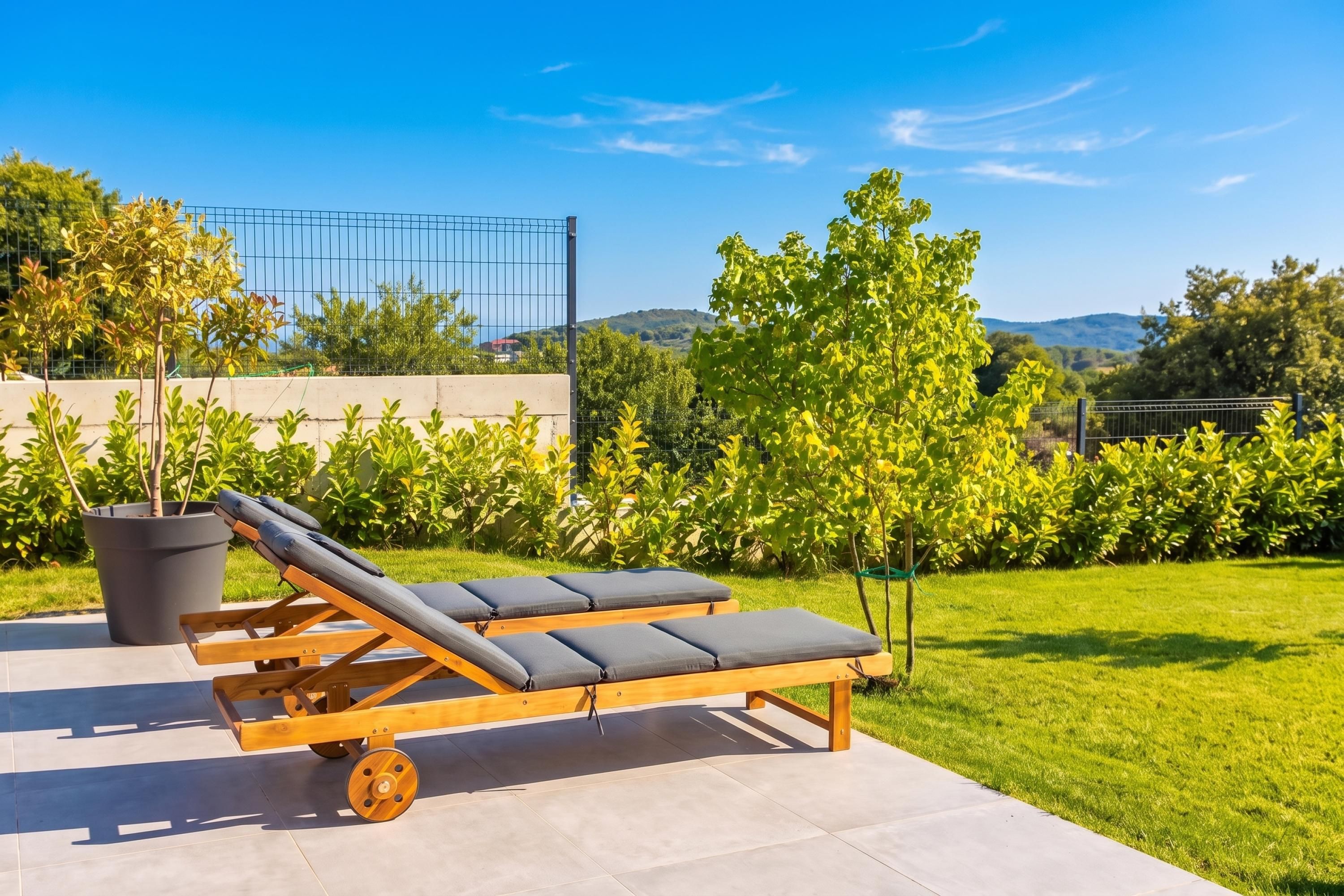 A sun lounger with wheels on a patio, surrounded by greenery and a clear sky.