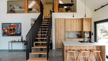 A modern kitchen with wooden cabinets, a central island with stools, and a staircase with black railings.