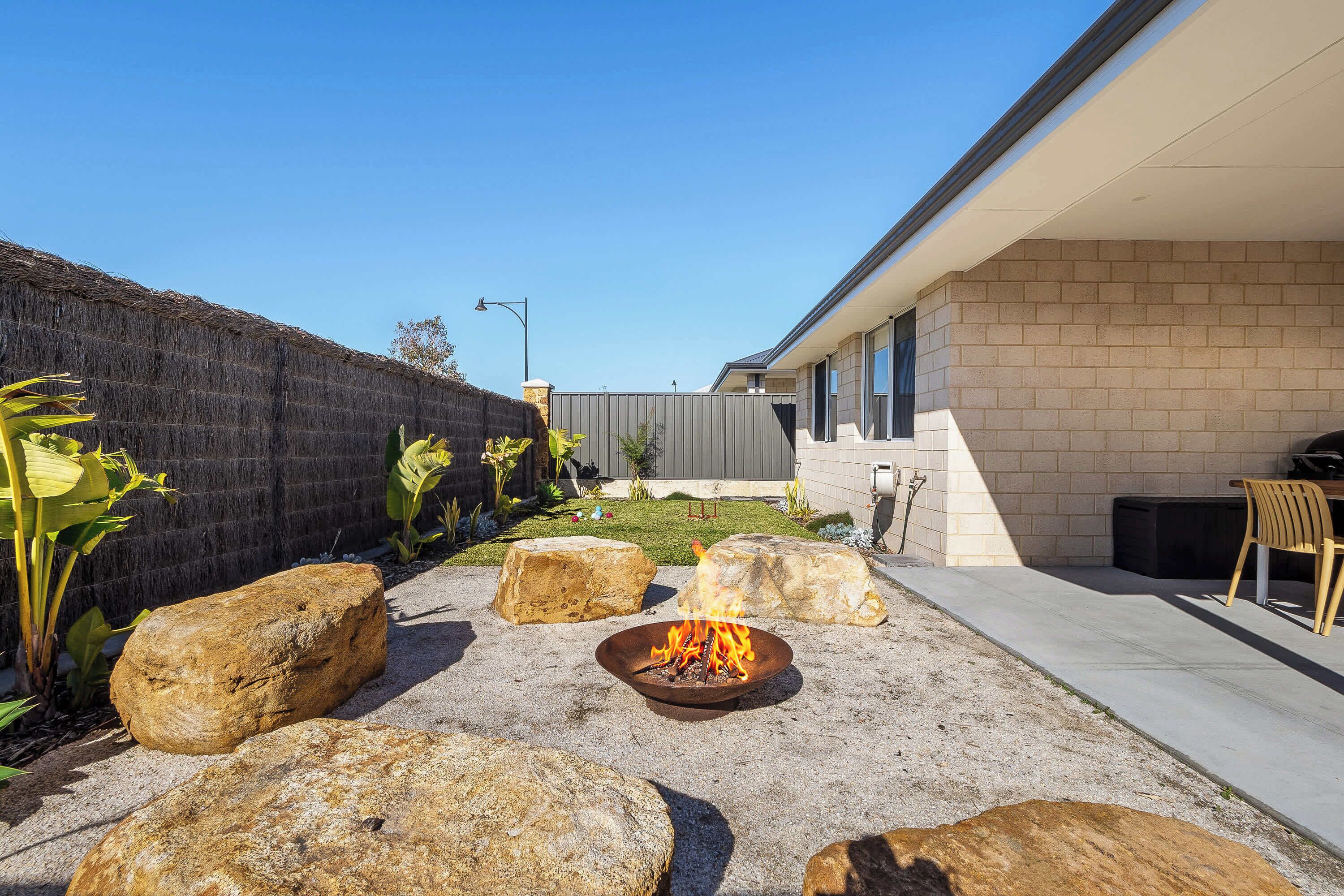 A backyard with a fire pit, large rocks, and a patio area with a chair.