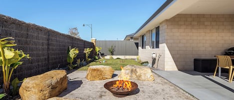 Patio trasero con un hoyo de fuego, rocas grandes y una zona de estar con una silla.